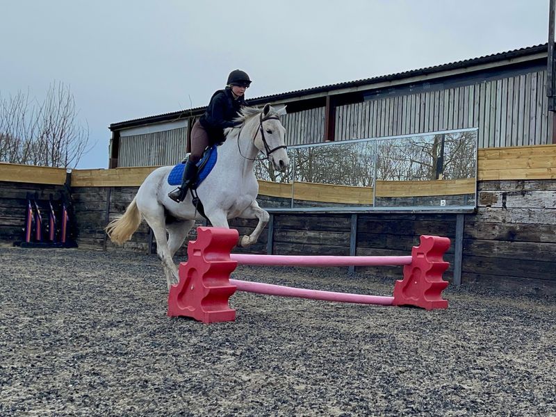 A young rider and pony jumping in an outdoor arena