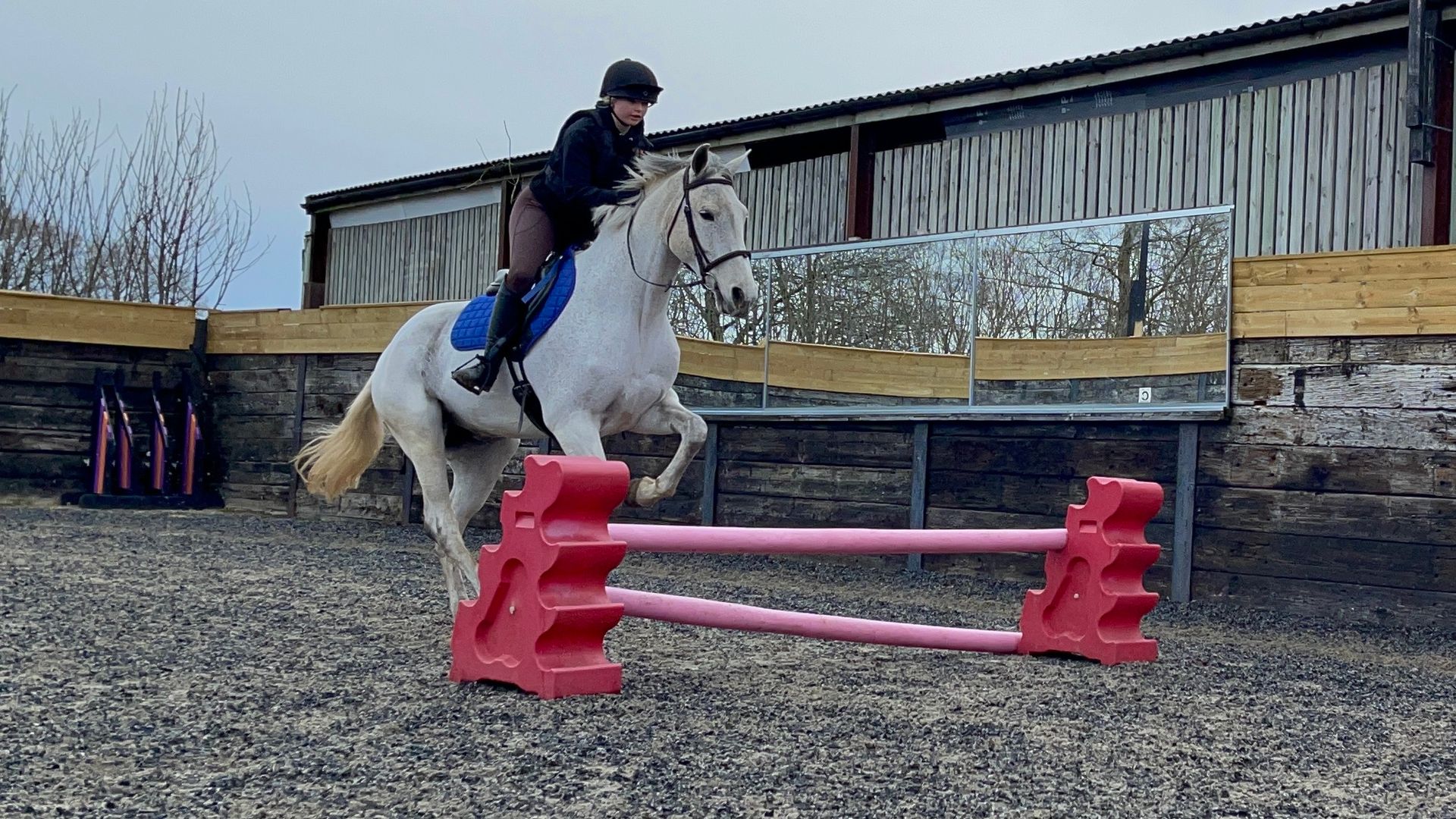 A young rider clearing a jump on a grey pony